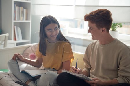 Photo for Two caucasian teenagers sitting back to back on floor and learning from books with smile - Royalty Free Image