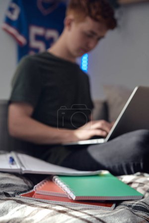 Photo for Caucasian teenager boy sitting on bed and learning using laptop - Royalty Free Image