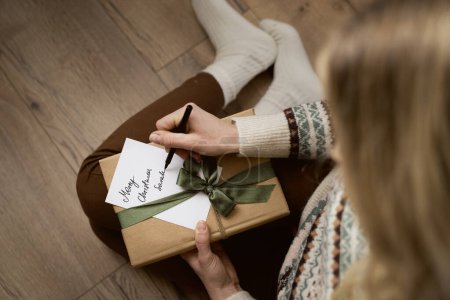 Draufsicht einer kaukasischen Frau, die auf dem Boden sitzt und Weihnachtskarten schreibt 