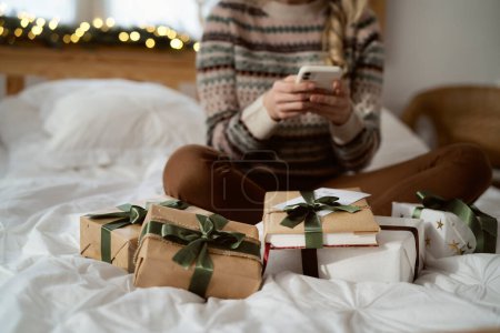 Unerkennbare Kaukasierin telefoniert im Bett zwischen Weihnachtsgeschenken
