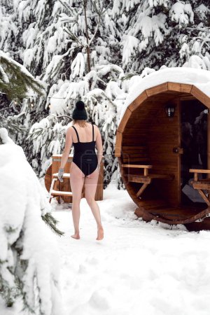 Foto de Caucasian woman going into the barrel with cold water in winter outdoors - Imagen libre de derechos