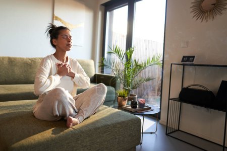 Foto de Mixed race woman meditating at home with eyes closed - Imagen libre de derechos
