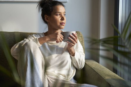 Foto de Mujer de raza mixta sentada en casa y disfrutando del café - Imagen libre de derechos