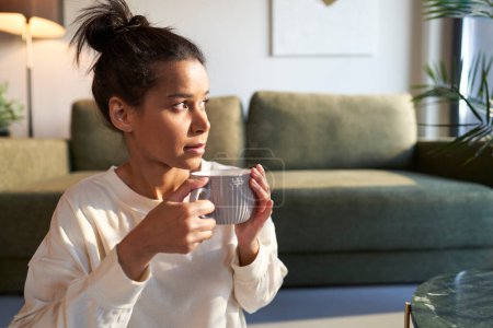 Photo for Mixed race woman sitting at home and enjoying the coffee - Royalty Free Image