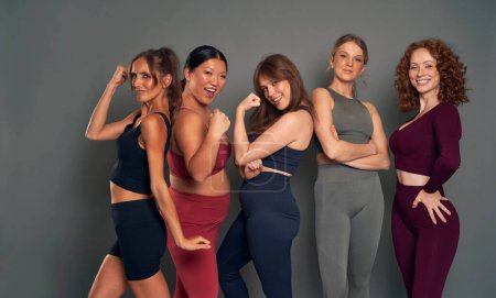 Foto de Grupo de felices cinco mujeres jóvenes mostrando fuerza en ropa deportiva - Imagen libre de derechos
