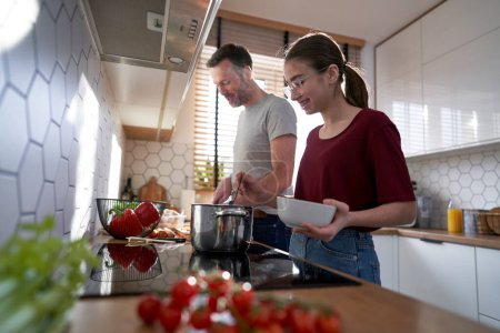 Photo for Caucasian man cooking with teenager daughter at home - Royalty Free Image