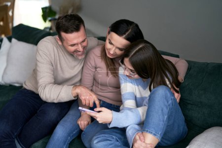 Photo for Caucasian family have fun together with mobile phone while relaxing at the sofa - Royalty Free Image