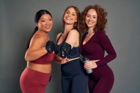 Téléchargez les photos : Three young women in sports clothes and gym accessories in studio shot - en image libre de droit