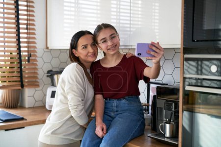 Photo for Caucasian mom with teenager daughter make a selfie in kitchen - Royalty Free Image
