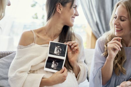 Téléchargez les photos : Caucasian pregnant woman showing the medical scan to her friends - en image libre de droit