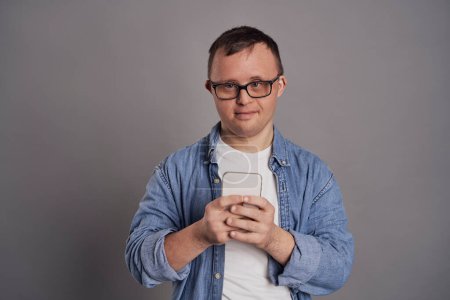 Téléchargez les photos : Homme adulte avec le syndrome du duvet en utilisant un téléphone mobile sur fond gris - en image libre de droit