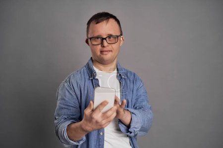 Téléchargez les photos : Homme caucasien avec le syndrome du duvet tenant téléphone mobile sur fond gris - en image libre de droit