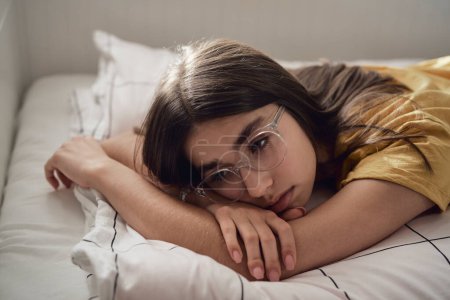 Photo for Sad caucasian teenage girl lying on bed and looking away with anxiety - Royalty Free Image