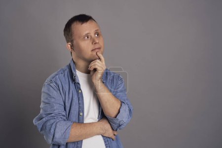 Photo for Man with down syndrome thinking about something on gray background - Royalty Free Image