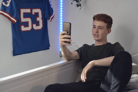 Téléchargez les photos : Caucasien adolescent garçon navigation téléphone tandis que assis sur le lit - en image libre de droit