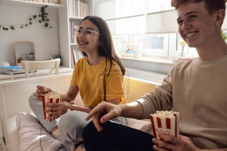 Photo for Two caucasian teenagers having fun while sitting on floor and eating popcorn - Royalty Free Image