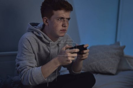 Téléchargez les photos : Adolescent caucasien garçon jouer sur game controller la nuit - en image libre de droit