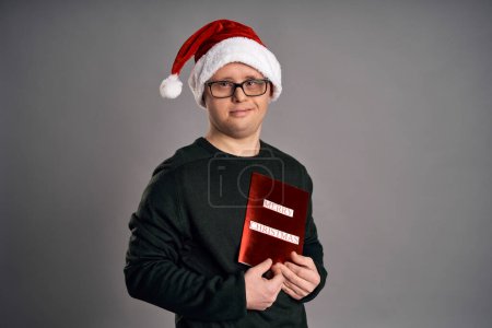 Téléchargez les photos : Homme avec le syndrome du duvet tenant carte de Noël avec des souhaits sur fond gris - en image libre de droit