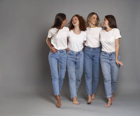 Téléchargez les photos : Quatre jeunes femmes caucasiennes marchant en jeans bleus et tshirt blanc sur fond gris - en image libre de droit