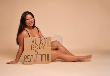 Photo for Chinese women in underwear sitting on nude background in studio and holding banner - Royalty Free Image