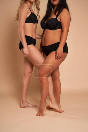 Photo for Two women in black underwear standing back to back and smiling towards the camera - Royalty Free Image