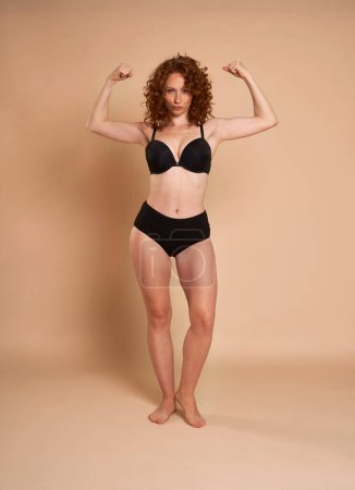 Photo for Caucasian  red head woman in black underwear showing muscles with her hands up - Royalty Free Image