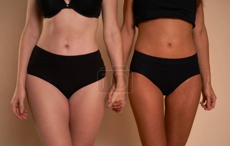 Photo for Two unrecognizable women in black underwear standing and holding hands - Royalty Free Image