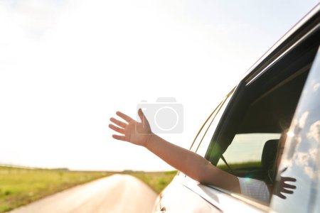 Téléchargez les photos : Enfant méconnaissable montrant la main hors de la voiture en marche - en image libre de droit
