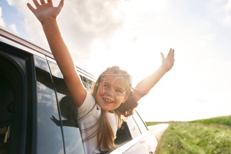 Téléchargez les photos : Caucasienne fille de huit ans regardant par la fenêtre de la voiture avec les bras tendus - en image libre de droit