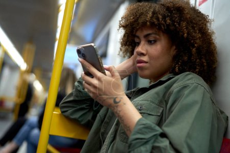 Foto de Joven mujer afro viajando por metro y navegando por un teléfono móvil - Imagen libre de derechos
