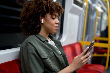 Téléchargez les photos : Jeune femme afro voyageant en métro et naviguant sur un téléphone mobile - en image libre de droit