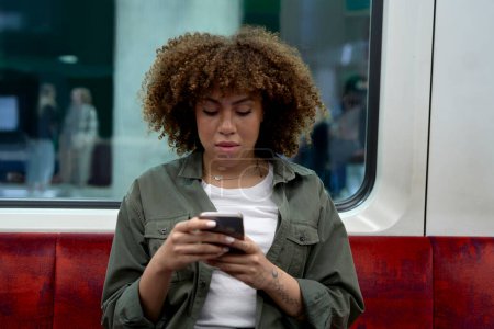Téléchargez les photos : Jeune femme afro voyageant en métro et naviguant sur un téléphone mobile - en image libre de droit