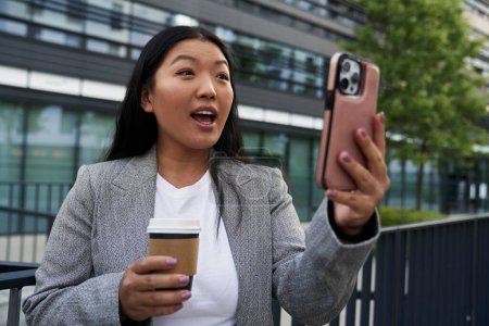 Téléchargez les photos : Femme chinoise d'affaires ayant un appel vidéo à côté du bâtiment - en image libre de droit