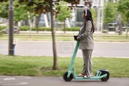 Foto de Mujer de negocios china montando en scooter push y escuchando música - Imagen libre de derechos