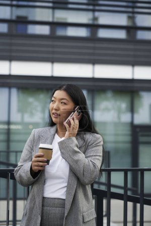 Téléchargez les photos : Femme chinoise d'affaires ayant un appel à l'extérieur et tenant une tasse de café - en image libre de droit