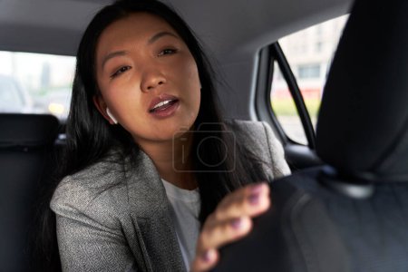 Photo for Chinese business woman driving in the taxi and asking driver about something - Royalty Free Image