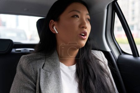 Téléchargez les photos : Femme chinoise d'affaires conduisant dans un taxi et faisant un appel téléphonique avec des écouteurs - en image libre de droit