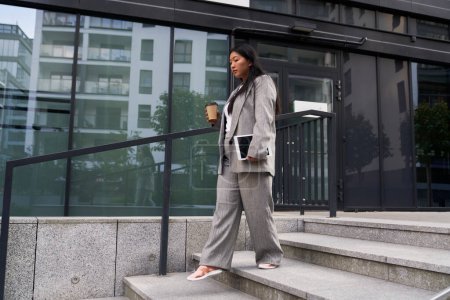 Foto de Mujer china de negocios caminando por la ciudad y sosteniendo una taza de café y mesa digital - Imagen libre de derechos