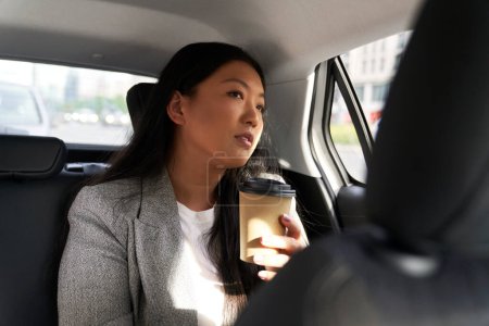 Photo for Business Chinese woman driving in a taxi and holding a cup of coffee - Royalty Free Image