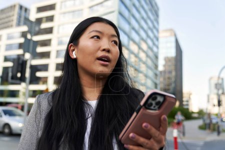 Téléchargez les photos : Femme chinoise d'affaires portant des écouteurs et appelant dans la rue - en image libre de droit