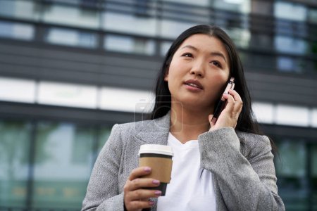 Photo for Business Chinese woman having a call and holding a cup of coffee - Royalty Free Image