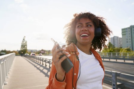 Foto de Mujer negra con auriculares y caminando por el puente - Imagen libre de derechos