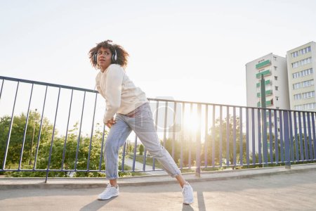 Téléchargez les photos : Plan large de la femme noire portant des écouteurs et dansant sur le pont - en image libre de droit