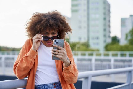 Téléchargez les photos : Femme noire portant des lunettes de soleil et regardant son téléphone portable - en image libre de droit