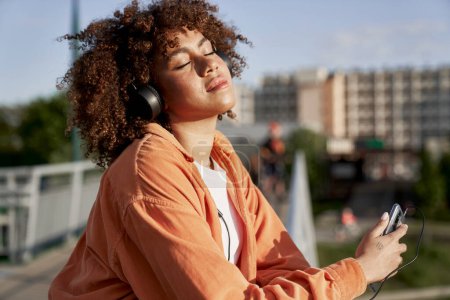 Foto de Mujer negra con auriculares y escuchando música durante el atardecer - Imagen libre de derechos