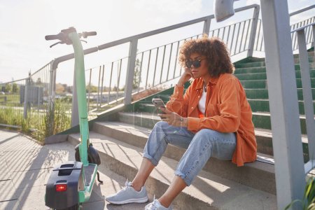 Foto de Mujer negra sentada en escaleras al aire libre y navegando por el teléfono móvil - Imagen libre de derechos