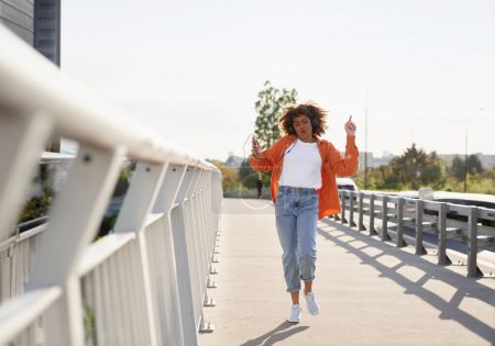 Photo for Wide shot of black woman wearing headphones and dancing on the bridge - Royalty Free Image