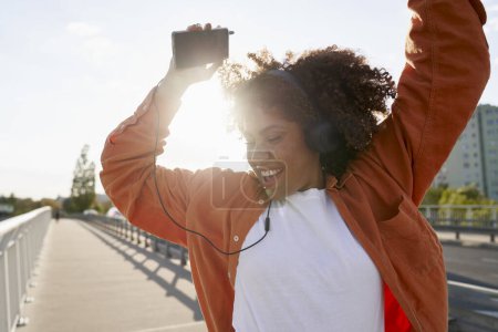 Photo for Close up of black woman wearing headphones and dancing on the bridge - Royalty Free Image