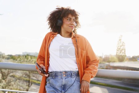 Téléchargez les photos : Femme noire portant des écouteurs et debout sur le pont - en image libre de droit