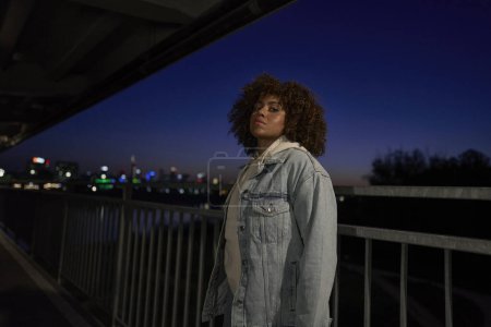 Téléchargez les photos : Portrait de femme noire debout sur le pont la nuit et regardant la caméra - en image libre de droit